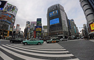 Taxis und Autos die über die Shibuya Kreuzung in Tokyo fahren. Fußgänger haben rot.